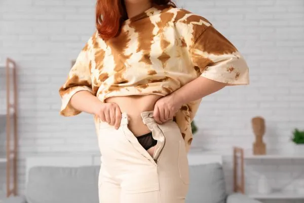 Image of woman trying to do her trousers up after pregnancy weight gain Kingshurst