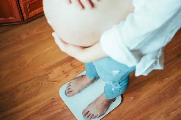 Image of woman weighing herself and experiencing weight gain through pregnancy Kingshurst